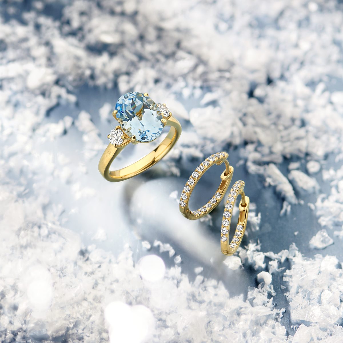 Gouden ring met lichtblauwe steen en twee gouden oorringen op sneeuw